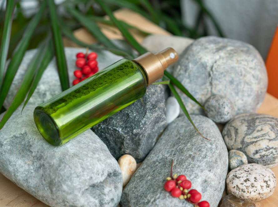 A bottle of green color with a spray bottle lies on the stones, next to the green leaves