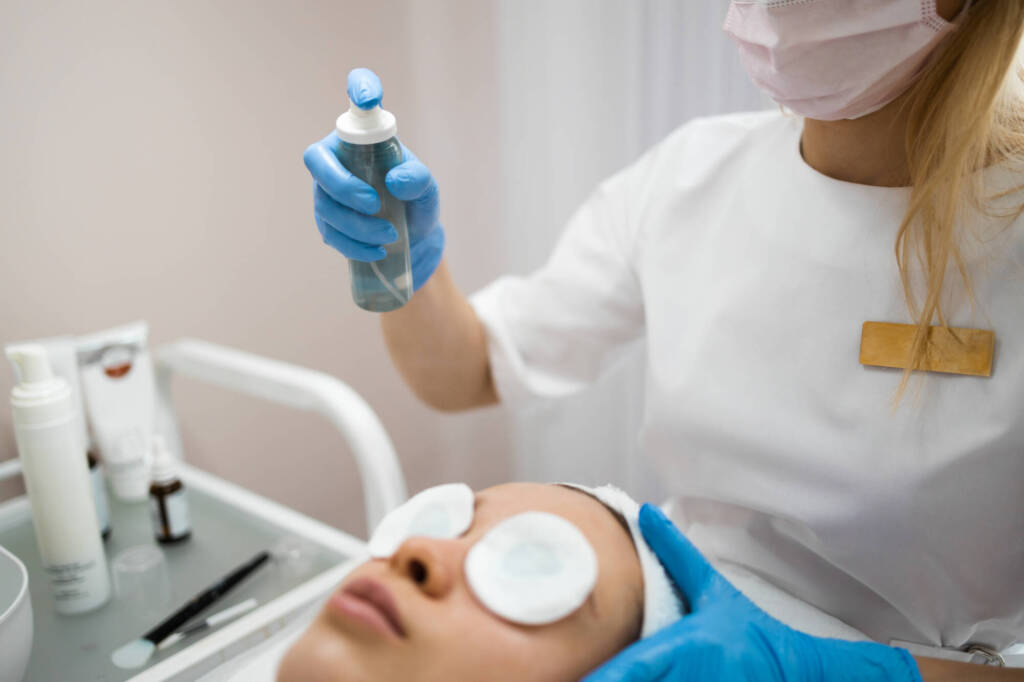 Beautician sprays cosmetic product on woman's face after the procedure.