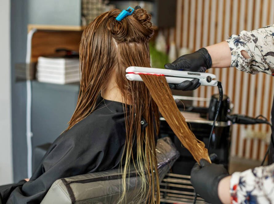 Professional hairdresser straightening long hair using straightener. Hair keratin.