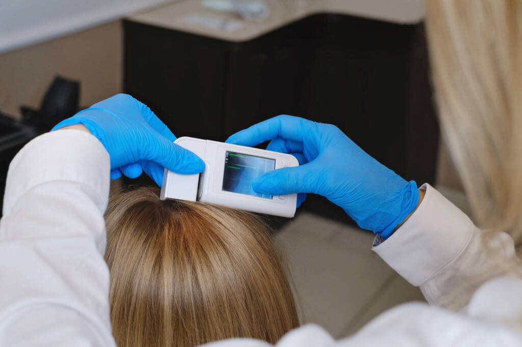 Trihologist examines head skin of woman with special dermatology equipment